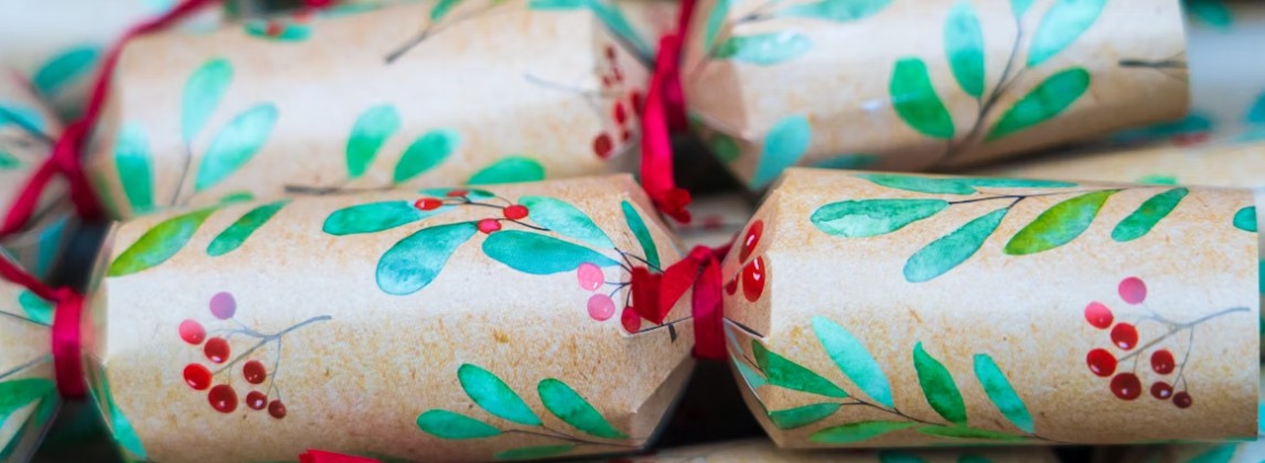 Julpyssel med handgjorda smällkarameller inslagna i brunt papper med gröna blad och röda bär, dekorerade med röda sidenband.